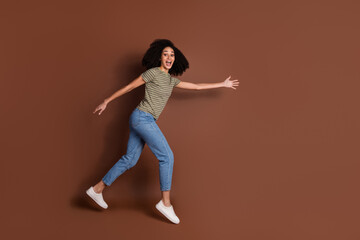 Full length photo of adorable lovely girl wear khaki t-shirt running jumping high empty space isolated brown color background
