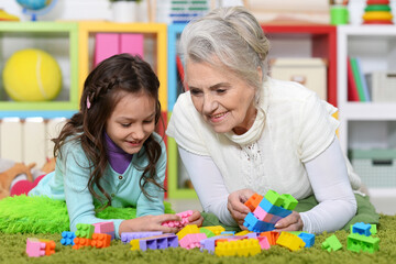 Fototapeta premium Cute girl and grandmother playing with colorful plastic blocks