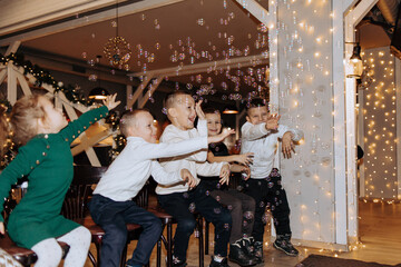 A group of children are playing with bubbles in a room. Scene is joyful and playful, as the children are laughing and having fun with the bubbles