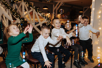 A group of children are playing with bubbles in a room with Christmas decorations. Scene is joyful and festive
