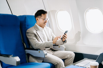 Young Asian executive excels in first class, multitasking with digital tablet, laptop and...