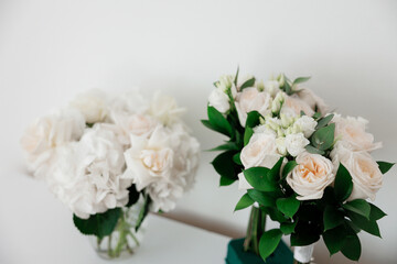 Two vases of flowers sit on a table, one of which is taller than the other. The flowers are white and green, with some of them having leaves