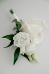 A bouquet of white flowers with green leaves. The flowers are arranged in a way that they look like they are pinned to a man's lapel