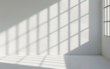 Obraz premium Sunlight streaming through large industrial-style windows, casting geometric shadows on a white wall in a minimalist, modern interior space.