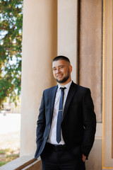 A man in a suit and tie stands on a balcony, smiling for the camera. Concept of confidence and professionalism, as the man is dressed in a formal attire and he is posing for a photo