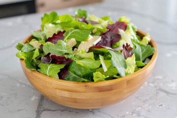 A wooden bowl filled with a colorful green salad made of fresh, leafy greens. The bowl is placed on a modern kitchen countertop.