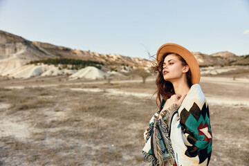 Desert wanderlust woman in hat and blanket standing amidst mountains in the arid landscape