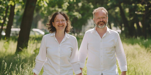 Middle-aged couple walking in park, holding hands, smiling, enjoying nature, autumn and summer settings, casual clothing, relaxed atmosphere