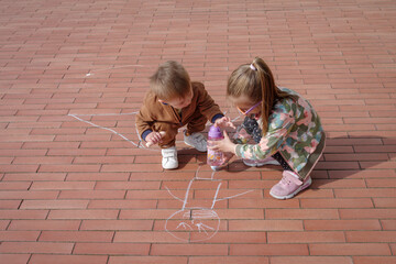 Little girl and boy scribbling in colourful chalk on pavement