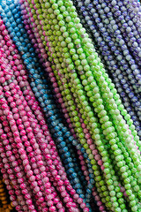 Close up of colorful beaded necklaces in various shades of pink, blue, green, and purple, arranged in rows.
