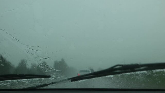 View through running car windshield during heavy rain. Wiper is cleaning windshield glass. Traffic on highway rain in rainy season. slow motion. rainfall on highway, dangerous weather conditions road