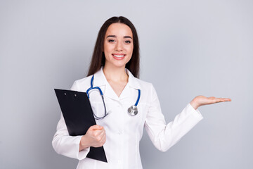Portrait of qualified doctor woman hold clipboard empty space white coat isolated on grey color...