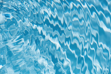 Blue water with ripples on the surface. Defocus blurred transparent blue colored clear calm water surface texture with splashes and bubbles. Water waves with shining pattern texture background.