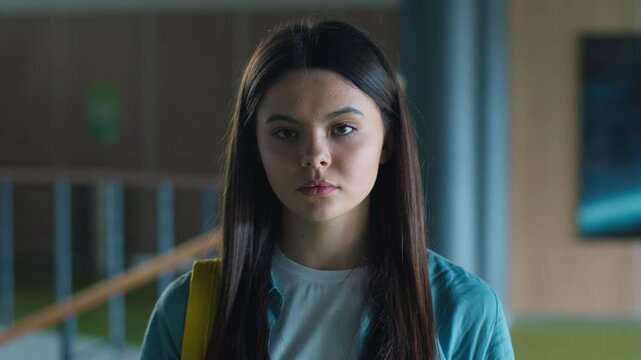 Portrait serious calm sad upset Caucasian student girl female schoolgirl woman pupil teenager teen teenage generation in school corridor in university college hall education study looking at camera