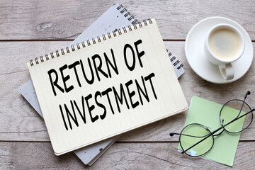 return on investment ( ROI ) text on a sheet of notepad near a cup of coffee