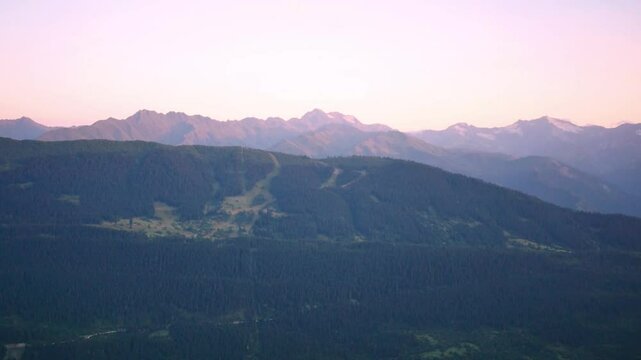 Panorama of pink sunrise in the mountains. Green hills and snowy peaks in the sun.