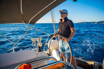 Young man captain stands at the helm and controls a sailboat during a journey by sea
