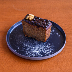 Delicious slice of banana bread topped with chocolate icing and a walnut, dusted with icing sugar on