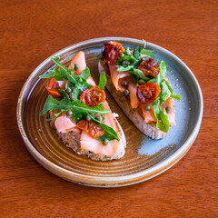 Two slices of delicious toast with smoked salmon, sun dried tomatoes and capers being served on a