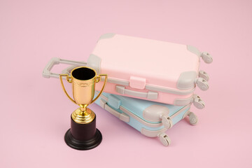 Gold champion cup and travel suitcases on pink background.