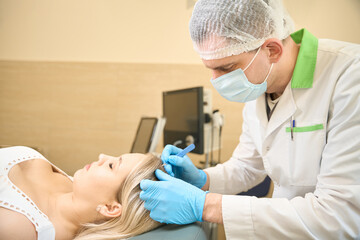 Dermatologic surgeon removing atheroma on female patient scalp using scalpel