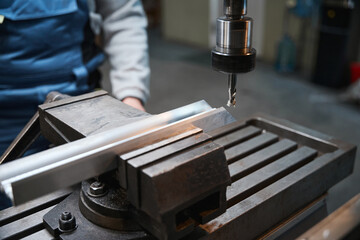 Worker drills a hole into an aluminum profile on machine