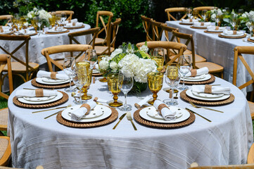 Round table with white tablecloth and wooden chairs being set for an outdoor wedding reception