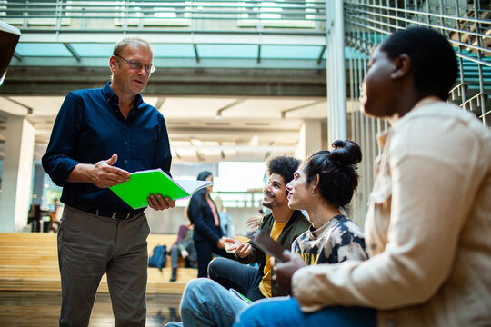 Professor discussing notes with diverse group of students in a modern university campus