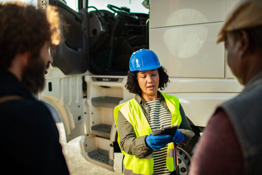 Female logistics manager with clipboard discussing with truck drivers