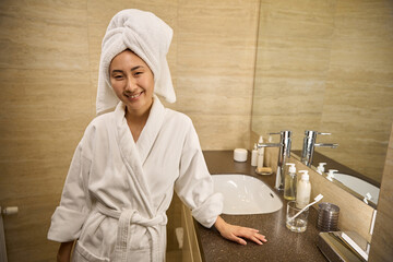 Relaxed Asian woman in bathrobe posing in spacious and comfortable bathroom