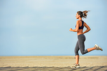 Attractive fit young woman running on Santa Monica Beach boardwalk pacific ocean in background