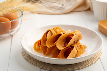 Pancake rolls stuffed with custard and sausage on white plate.popular street snack in Thailand call 