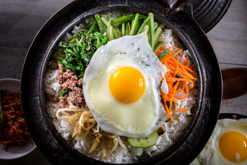 Bibimbap with variety of vegetables and fried egg top view in ceramic bowl.