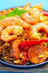 A black pan filled with a variety of food including shrimp, peppers, and corn