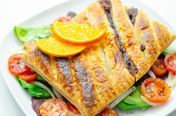 A plate of food with a pastry and a slice of orange on top