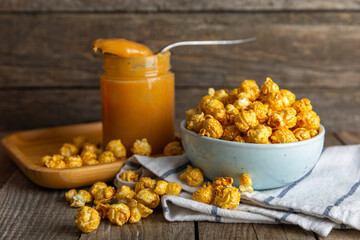 Sweet caramel popcorn in a bowl on a wooden background. Salted caramel popcorn. Caramel sauce. Close up. Topping. Place for text. Copy space