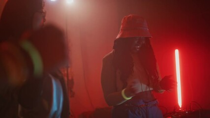 Handheld lowkey shot of diverse female best friends in fancy retro outfits moving to electronic dance music and raving during y2k party in red neon lit nightclub