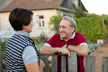 Two gardeners friendly talking outdoors next to wooden fence of country estate on day