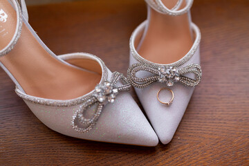 A pair of silver high heels with a bow on the front and a ring on the back. The shoes are on a wooden surface