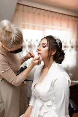 A woman is getting her makeup done by a woman in a white robe
