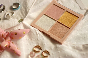White blouse, denim skirt, colorful rings, earrings and beauty products on white background. Summer outfit in pastel colors. Selective focus.