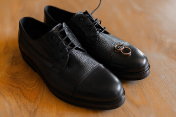 A pair of black shoes with a ring on the left shoe. The shoes are on a wooden table