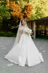 A woman in a white wedding dress is standing in front of a building with a white canopy. She is holding a bouquet of flowers