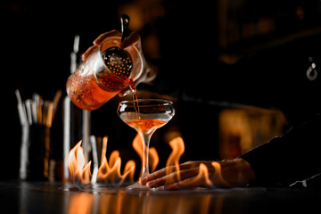 Professional bartender making drink in cocktail glass with alcohol fire flame