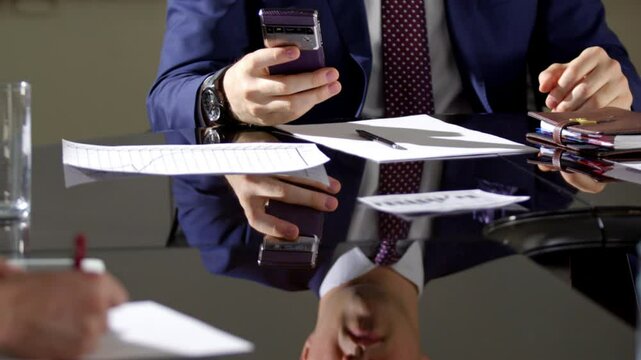 Manager sits near black glossy table at meeting crop body. Male checks cell phone stands up and goes away from office chair