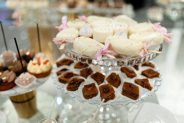 A dessert table with a variety of treats including cakes, cookies, and brownies. The table is set with a clear glass platter and a few decorative items such as a pink ribbon and a gold stand