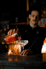 Master with black short hair making a cocktail in a fired wood bar counter