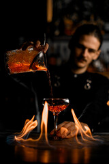 Guy with neat mustache in black shirt stands behind a fired wood bar counter