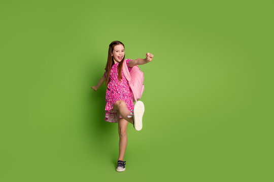 Full size photo of cute schoolgirl dance empty space wear pink dress isolated on green color background