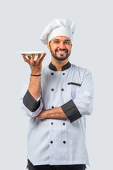 Indian asian young Chef in uniform happily presenting empty white ceramic plate on white background